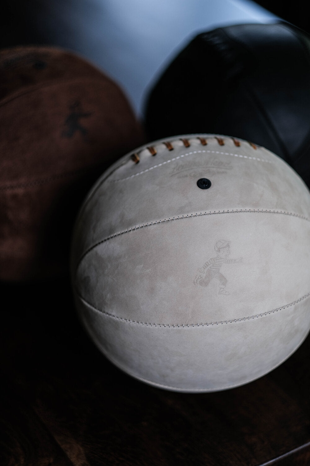 Taupe nubuck Run Boy basketball with embossed running-boy logo, displayed beside darker leather balls